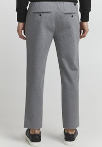 Grå, strukturerede bukser med to baglommer og dekorativ syning. Båret med sorte sneakers, der fremhæver en lige ben-design.