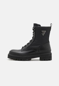 Bottines noires à lacets avec une semelle épaisse, finition en cuir lisse et un accent logo triangulaire sur le côté. Semelle extérieure en caoutchouc texturé.