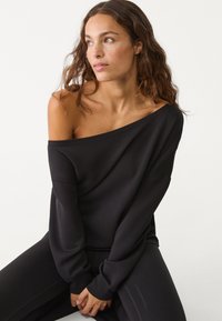 Schwarzer schulterfreier Pullover aus einem weichen, dehnbaren Stoff. Verfügt über lange Ärmel und eine lockere Passform, ergänzt durch passende schwarze Hose.