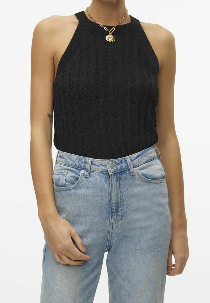 Czarny dzianinowy top bez rękawów z prążkowanym dekoltem, w zestawie z wysoko osadzonymi jasnoniebieskimi dżinsami o luźnym kroju i subtelnych przetarciach.
