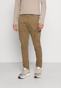 Khaki spodnie cargo o slim fit, z wieloma kieszeniami i trwałej tkaninie bawełnianej. W połączeniu z jasnoszarymi i beżowymi butami sportowymi.