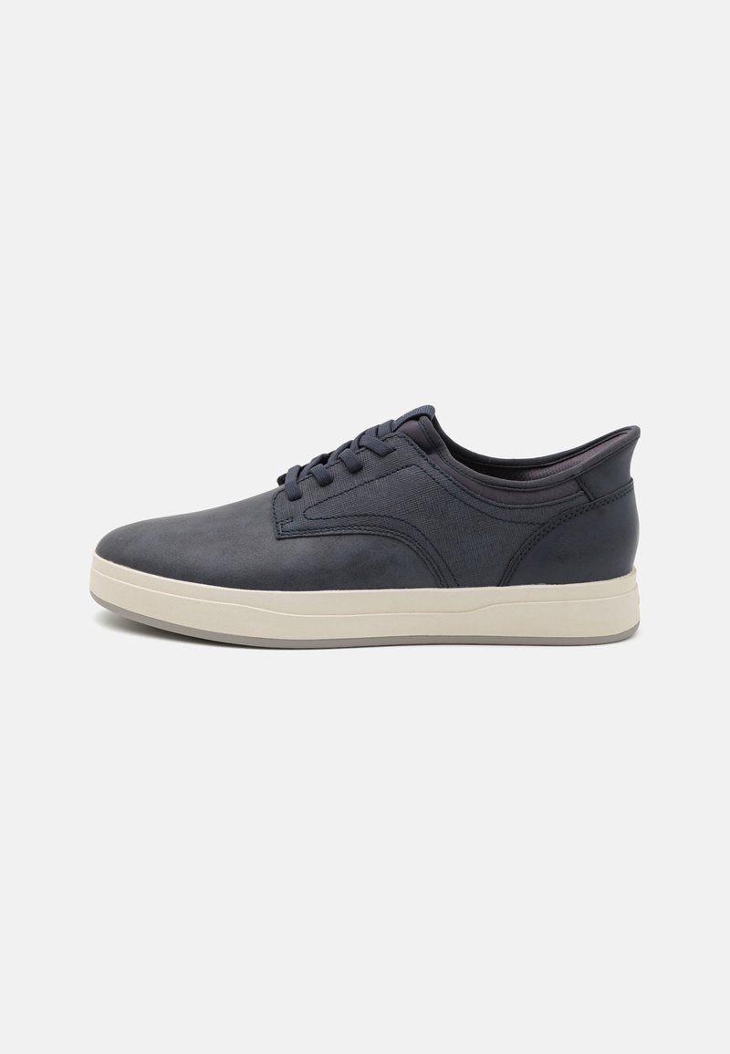 Navy blue sneakers with a smooth finish, rounded toe, and cream rubber sole. Features six eyelets and subtle side stitching detail.