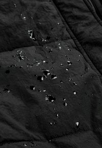 Schwarzer isolierter Jackenstoff mit sichtbaren Wassertropfen auf der Oberfläche, der ein strukturiertes, gestepptes Design zeigt und die wasserdichten Eigenschaften verstärkt.