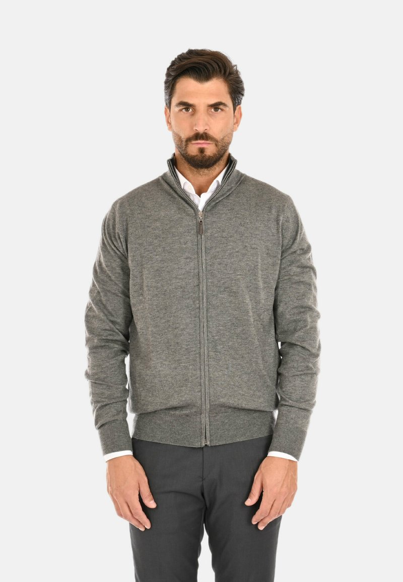 Maglione grigio con zip e alto collo, con polsini e orlo a costine. Presenta una trama liscia ed è indossato sopra una camicia bianca con colletto.