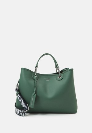 Sac à main en cuir vert foncé avec deux poignées et une bandoulière en tissu noir ornée d'un logo blanc en lettres majuscules.