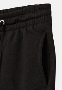 Schwarze Baumwoll-Jogginghosen mit elastischem Taillenbund und Kordelzug, seitlichen Taschen und strukturierter Stoffoberfläche.