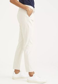 Bežové nohavice slim fit s plochým predným dielom a bočnými vreckami, skombinované s bielymi teniskami. Hladká tkanina a strih po členky.