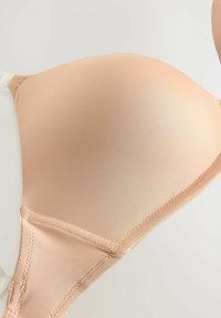 Beige beha met padding en een gladde, ribbelige textuur. Voorzien van verstelbare bandjes en stiksel details langs de randen voor ondersteuning en structuur.