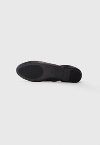 Black leather dress shoe shown from sole view with textured rubber grips on a white background.