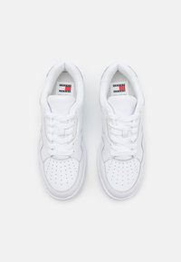 Zapatillas de cuero blanco con una caja de dedo perforada, cordones planos y una pequeña etiqueta de logo en el interior. Suela acolchada y acentos texturizados en los lados.