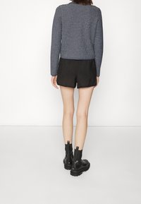 Pitkähiha, tummansininen teksturoitu neule lyhyellä mitoituksella, yhdistettynä korkeavyötäröisiin mustiin shortseihin ja mustiin nilkkabootseihin, joissa on paksu pohja.