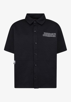 Chemise noire à manches courtes avec boutons, ornée d'un motif texturé géométrique et d'un logo "JORDAN" blanc sur la poitrine gauche.