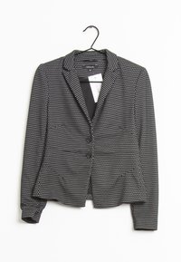 Mustavalkoisilla pilkuilla varustettu musta bleiseri, jossa on kaksi etupainiketta ja lovikäänteet. Valmistettu teksturoidusta kankaasta, ripustettuna koukkuun.