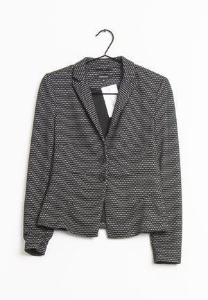 Blazer nero con pois bianchi, due bottoni frontali e rever a punta. Realizzato in tessuto testurizzato, appeso a un gancio.