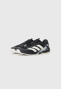 Chaussures de sport noires avec des rayures blanches, en matériau synthétique, avec un bout rond, un design à lacets et une semelle en caoutchouc texturée.