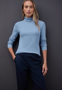 Jasnoniebieski, długi rękaw, golf w ribbowym wzorze, zestawiony z ciemnogranatowymi spodniami o kroju dopasowanym. Neutralne tło podkreśla stylizację.