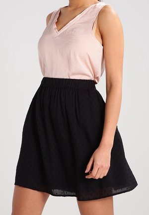 Frau trägt ein ärmelloses, hellrosa V-Ausschnitt-Oberteil, das in einen hoch taillierten, schwarzen, strukturierten knielangen Rock gesteckt ist.