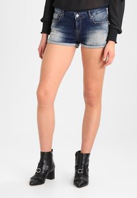 Jeansshorts i mörkblå färg med en ljus tvättseffekt, försedda med framfickor och en fransig nederkant. Matchas med svarta ankelstövlar med detaljer.