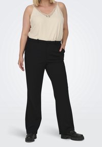 Beige linne med spetskant vid halsen, tillsammans med svarta, raka byxor med fickor och en slät textur. Svarta skor med tjocka sulor.