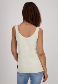 Witte gebreide tanktop met een V-hals en brede banden; geribbelde zoom. Geken met lichtblauwe jeans die een soepele textuur tonen.