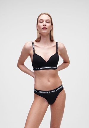 Black lingerie set featuring a seamless bralette with adjustable straps and logo band, paired with matching low-rise thong. Smooth fabric.