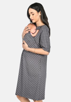 Grey maternity dress with white polka dots, short sleeves, and a pouch for holding an infant. Soft fabric and knee-length design.