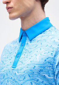 Jeune personne portant un polo à motifs bleus avec un col et une patte de boutonnage unis d'un bleu vif, visible du cou jusqu'à la poitrine.