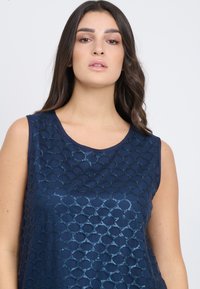 Top senza maniche di colore navy con un motivo testurizzato di cerchi intrecciati. Presenta un collo rotondo e una finitura in tessuto liscia.