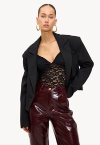 Zwarte oversized blazer gecombineerd met een zwart kanten body en glanzende bordeauxrode gepatineerde leren broek. Gouden creolen maken de look compleet.