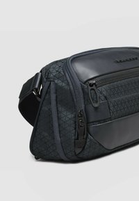 Borsa a tracolla in tessuto blu navy con motivo geometrico, dotata di pannello frontale in pelle, più tasche con cerniera e tracolla regolabile.