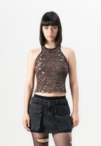Braunes Cropped Top mit einem einzigartigen Ausschnitt-Design, kombiniert mit einem schwarzen Denim-Rock mit großen Fronttaschen und einem breiten Taillenbund.