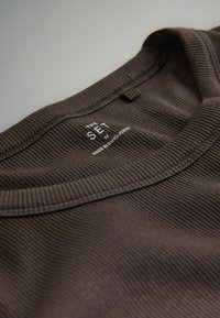 Brun ribbad t-shirt-hals med en synlig etikett som säger "THE SET M MADE IN BANGLADESH." Mjuk textur och enkel design.