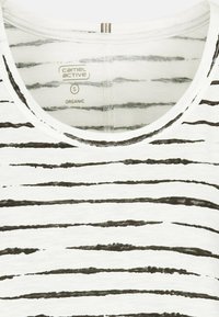 Biała koszulka z organicznej bawełny z czarnymi poziomymi paskami. Posiada okrągły dekolt i subtelną teksturę. Metka widoczna w okolicy kołnierza.