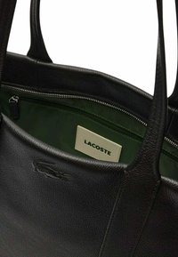 Sac fourre-tout noir en cuir Lacoste avec extérieur texturé, intérieur en tissu vert, poche zippée et détail du logo à l'avant.