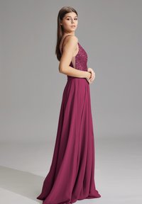 Langes, fließendes Kleid aus burgunderfarbenem Stoff. Das Mieder verfügt über ein eng anliegendes, glitzerndes Paillettendesign mit dünnen Trägern und einem schwingenden Rock.