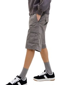 Grey cargo shorts with two side pockets and a patch pocket on each leg. Worn with black sneakers and grey socks. Cotton material.