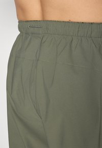 Olive green shorts with an elastic waistband, featuring a drawstring and smooth texture. Side pocket visible with flat seams.