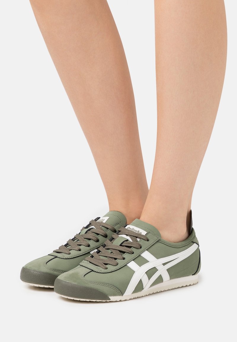 Zapatillas deportivas verdes con un acabado suave, franjas laterales blancas y cordones oscuros. La suela es texturada para mejorar la tracción.