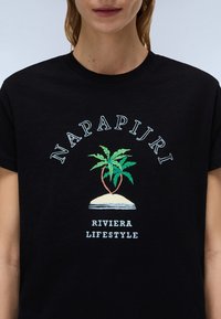 Juodas medvilninis marškinėlis su grafiniu spaudiniu, kuriame pavaizduoti palmės, paplūdimys ir tekstas "NAPAPIJRI RIVIERA LIFESTYLE" šviesiomis spalvomis.