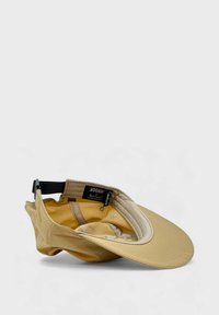 Moomin-lippis vaaleanbeigellä kankaalla, jossa on kaareva lippa. Varustettu säädettävällä mustalla hihnalla ja sisävuorella, jossa on kontrastia vaaleanruskea väri.