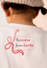 Felpa bianca in cotone con etichetta stampata con testo rosso: "a: minnie" e "da: Babbo Natale," accompagnata da un'illustrazione di un nastro rosso.