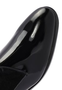 Chaussure en cuir verni noir avec une finition brillante, dotée d'un dessus lisse, d'un panneau latéral élastique et de coutures décoratives le long de la couture.