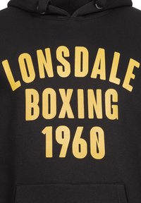 Čierna mikina s kapucňou s veľkým žltým nápisom "LONSDALE BOXING 1960." Obsahuje kapucňu na šnúrky a predné vrecko typu klokanka.