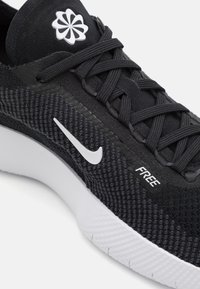 Sort atletiksko med en struktureret mesh-overdel, hvid sål, fremtrædende swoosh-logo og "FREE"-mærkat på siden.
