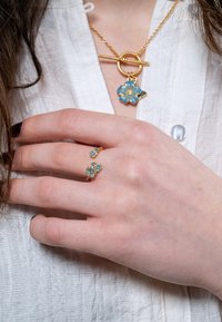 Kuldteest valmistatud ehted, millel on lilleline disain; kaelakee koos sinise lille ripatsiga ja sobiv sõrmus, millel on kaks väiksemat sinist lillekest sõrmel.