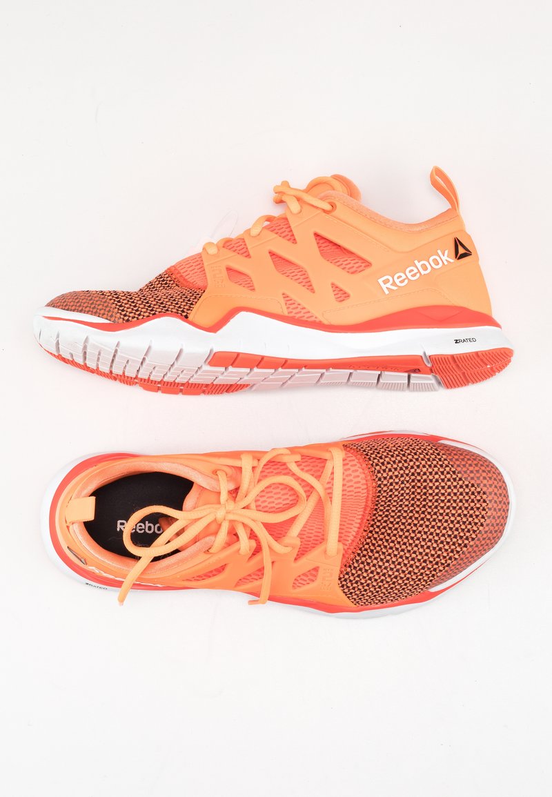 Sportovní boty Reebok v oranžové a korálové síťovině, s vzorovaným svrškem, bílou mezipodešví a vroubkovanou gumovou podešví pro trakci.