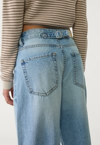 Vaaleansiniset, korkeavyötäröiset farkut, joissa on rento istuvuus, vyölenkit ja kaksi takataskua. Yhdistetty raidalliseen villapaitaan.