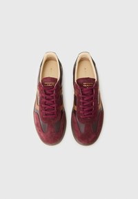 Burgunderfargede sneakers laget av semsket skinn og lær, rund tå, kontrasterende brune detaljer og tykke, teksturerte snørebånd.