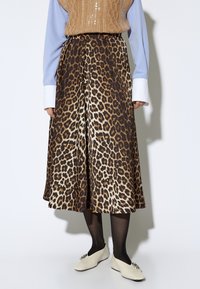 Falda plisada con estampado de leopardo en una paleta de colores marrón y crema, combinada con un chaleco de punto beige y una blusa blanca, llevada con medias negras y zapatos.