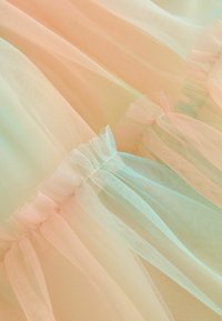 Tissu en tulle pastel présentant des teintes douces de pêche et de menthe, avec des volants froncés le long des bords, offrant une texture légère et aérienne.